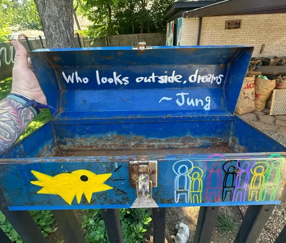 Magick Toolbox. An open blue metal toolbox painted with a yellow bird and outlined figures; the lid reads “Who looks outside, dreams” with a Jung attribution.