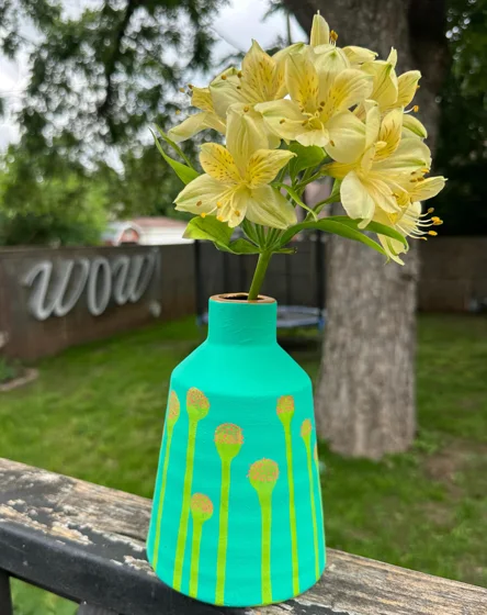 Painted vintage ceramic. A turquoise ceramic vase decorated with yellow lines and circles, photographed holding pale yellow flowers.