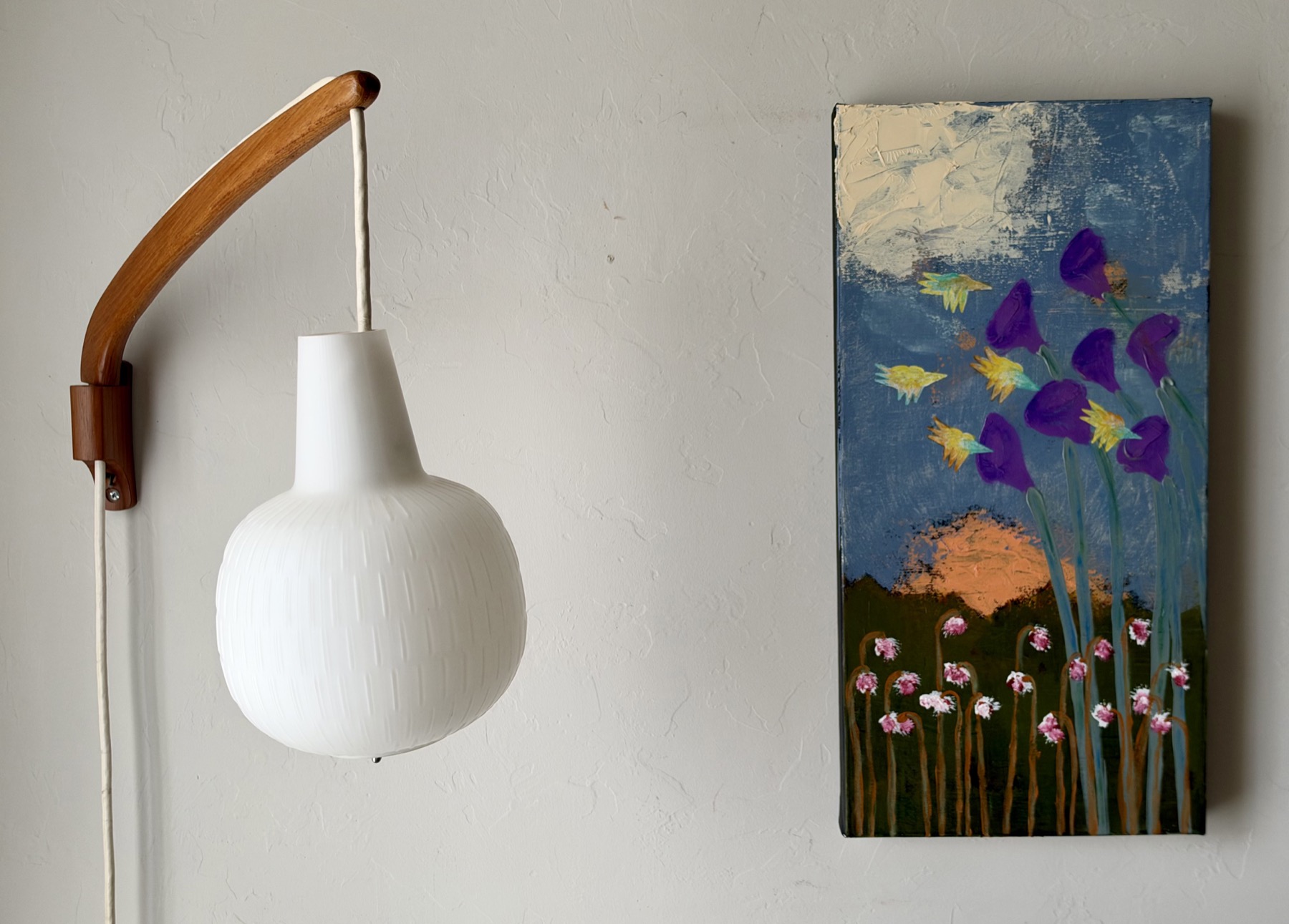 Over the Pass. A tall painting of yellow and turquoise hummingbirds among purple flowers above a mountain landscape, hanging beside a white pendant lamp.